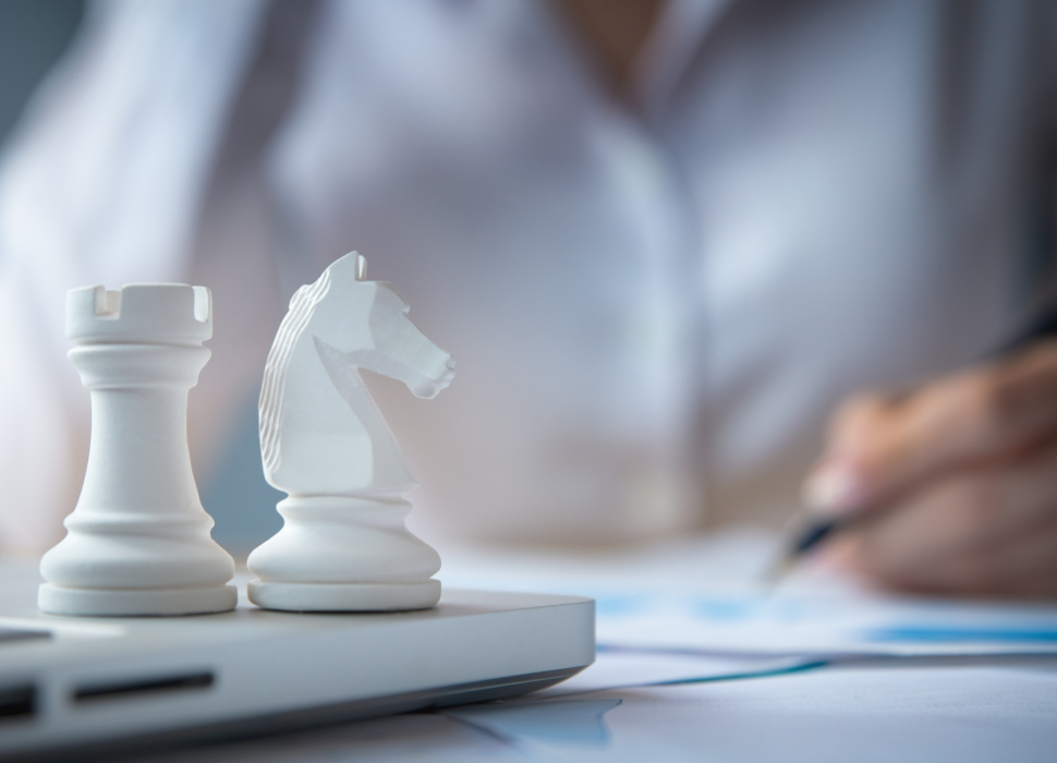 a closeup of a man writing a report and two chess pieces on top of a laptop